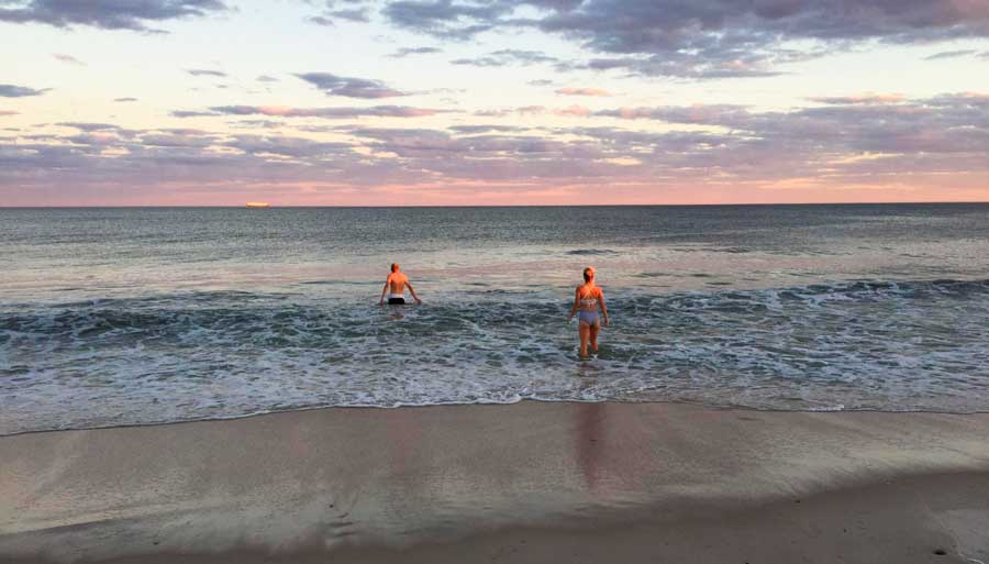 People enjoying their day in a beach and the colorful sky during sunset over it 