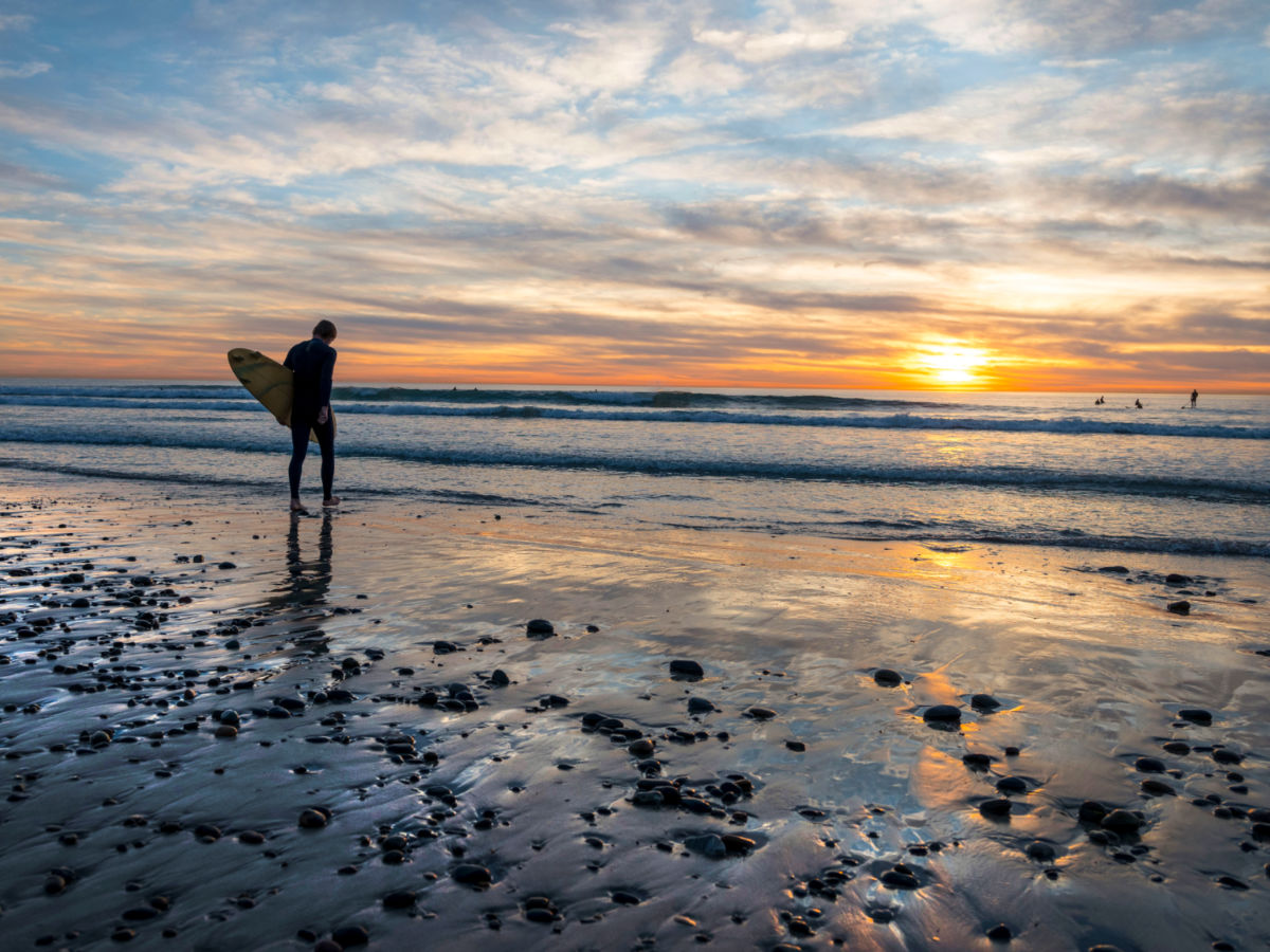 A surfer going to the ocean to catch a wave at Beacon’s Beach in Leucadia