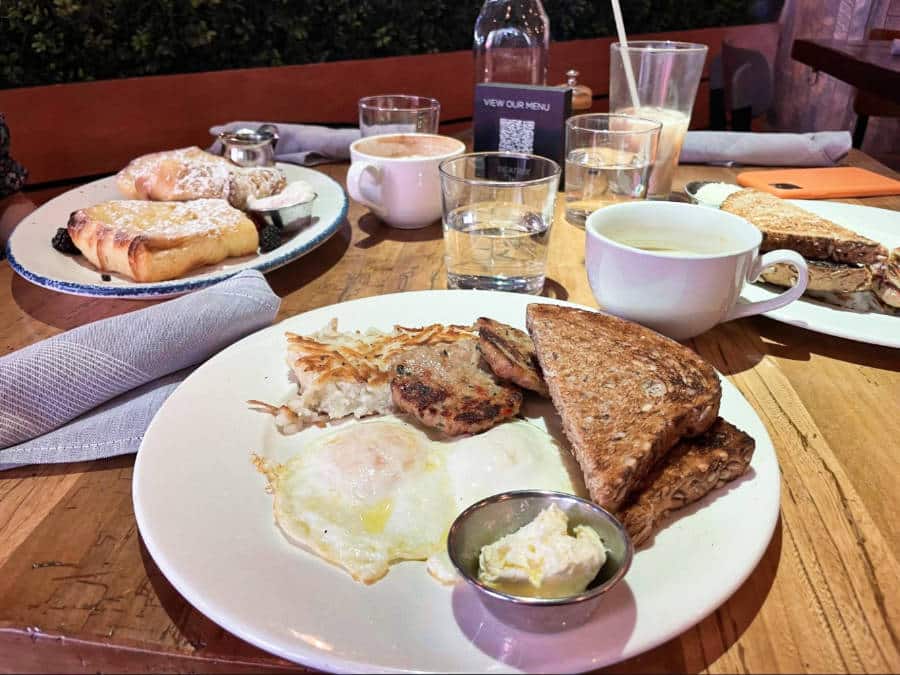 A plate of sliced toast bread, egg, burger patties, and hash browns with other breakfast meals on the table