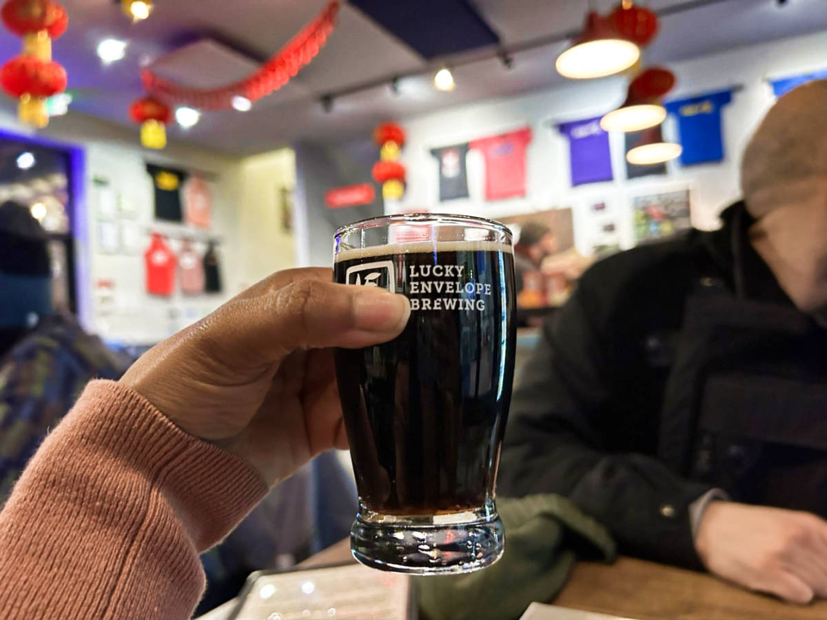 A hand holding a glass of beer from Lucky Envelope Brewing