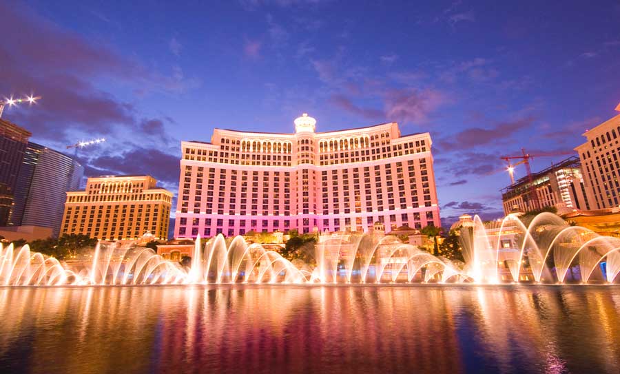 The Bellagio Hotel with lights at night and a water fountain on its foreground