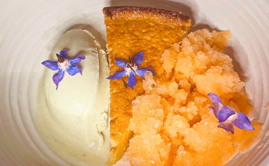 A slice of pie with cream on the side topped with edible flowers
