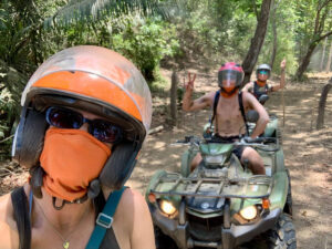 The author Betty Hurd, covering her face with neck gaiter while riding the ATV with her friends