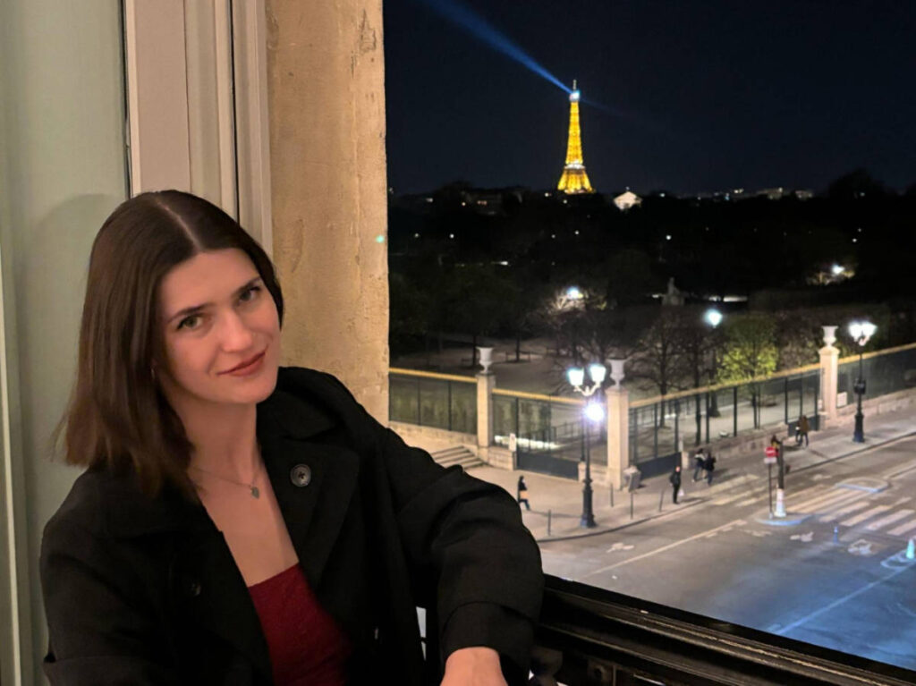 The author Betty Hurd sitting near the window with an overlooking view of the street and Eiffel Tower