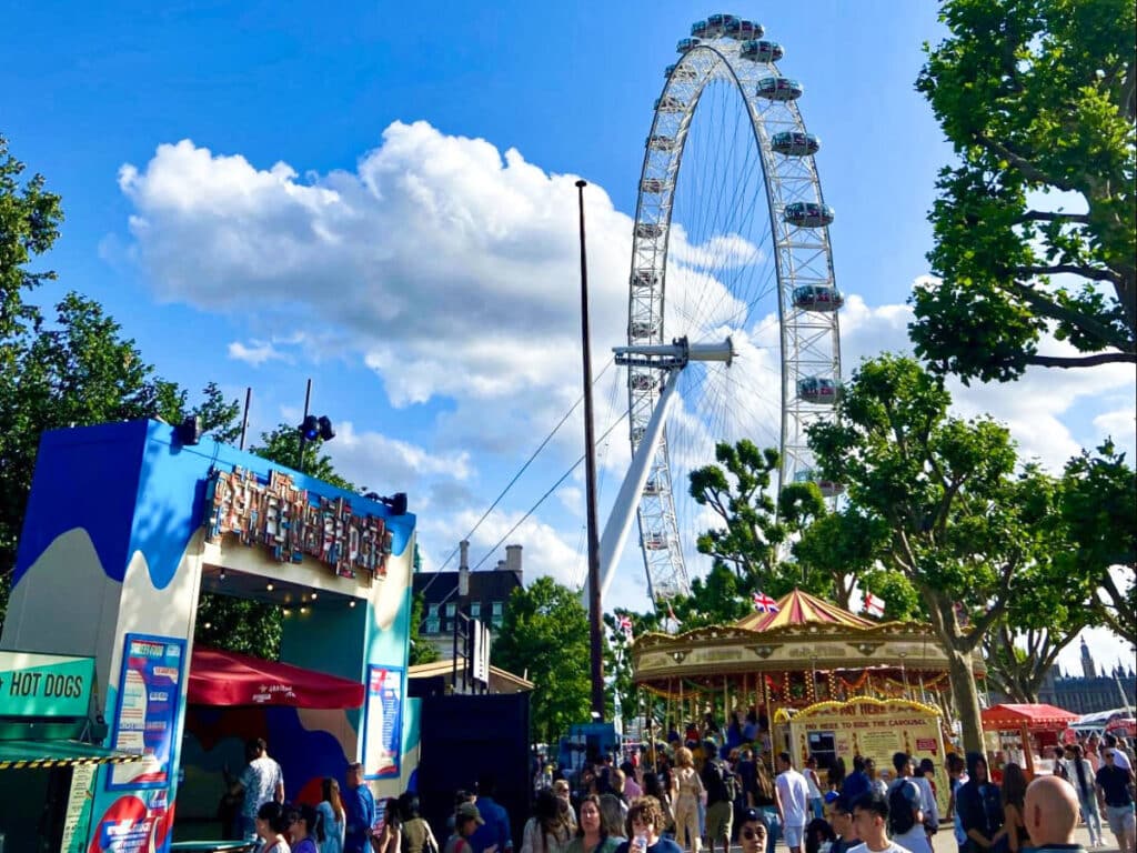 View of the crowd near the entrance of Between the Bridges with the carousel and London Eye in the background