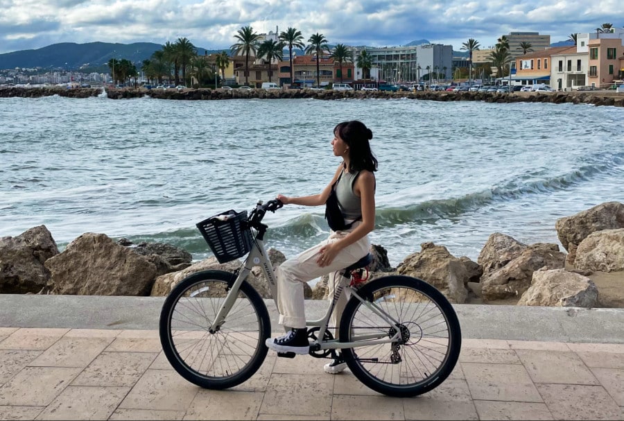 The author Lea Rose Allbaugh posing with a scenic background of the sea and town along Avenida de Gabriel Roca