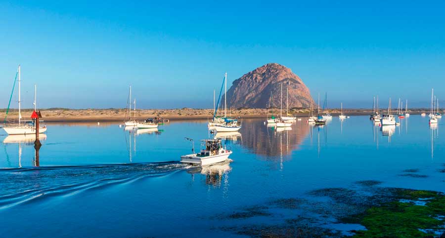 Boats on a harbor in Morro Bay and the Morro Rock from afar