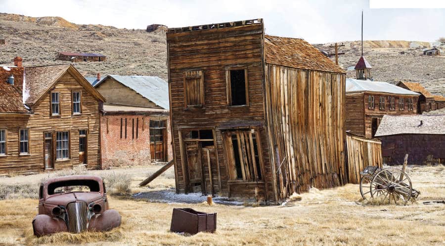 A rusty vintage car and abandoned wooden houses of Bodie's ghost town in California.