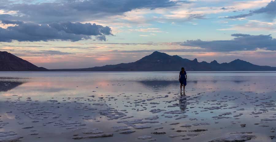 View of a woman in the Bonneville Salt Flats and her reflection on the water during sunset