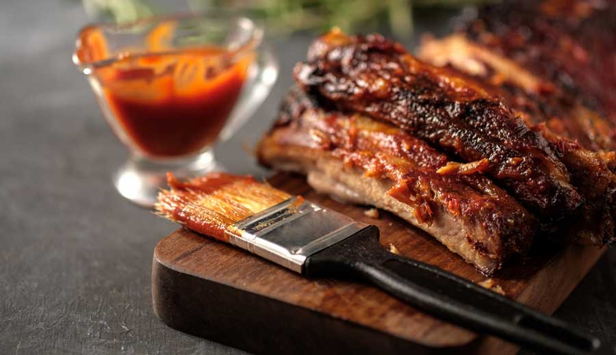 Close up view of a barbecue ribs on a wooden board with a brush beside it