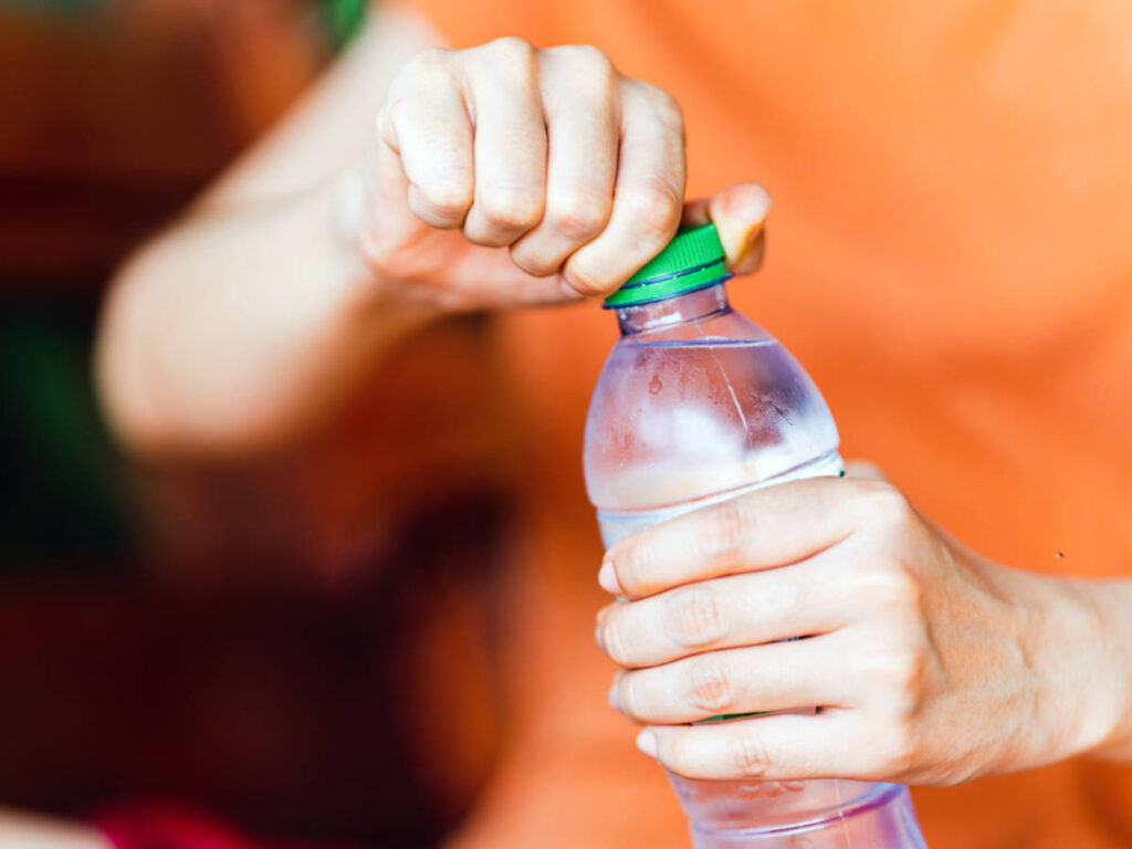 A hand opening the lid of the plastic water bottle