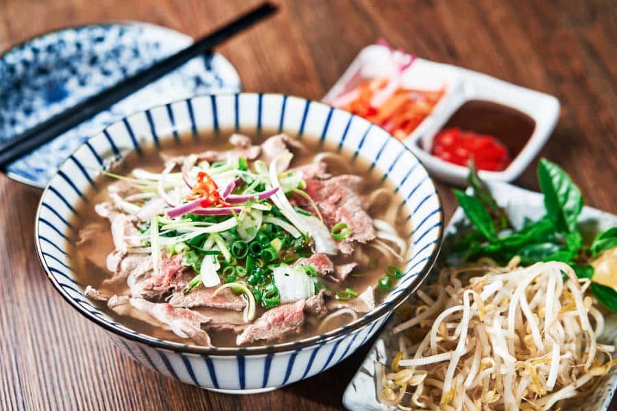 A bowl of beef pho with sauces and vegetables on the side