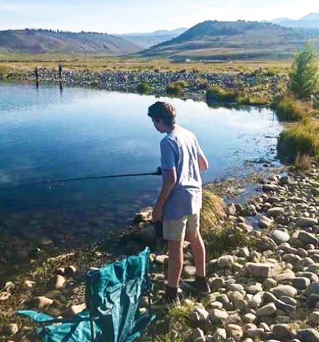 View of a boy fishing in Hayden Meadows Reservoir with a camping chair nearby