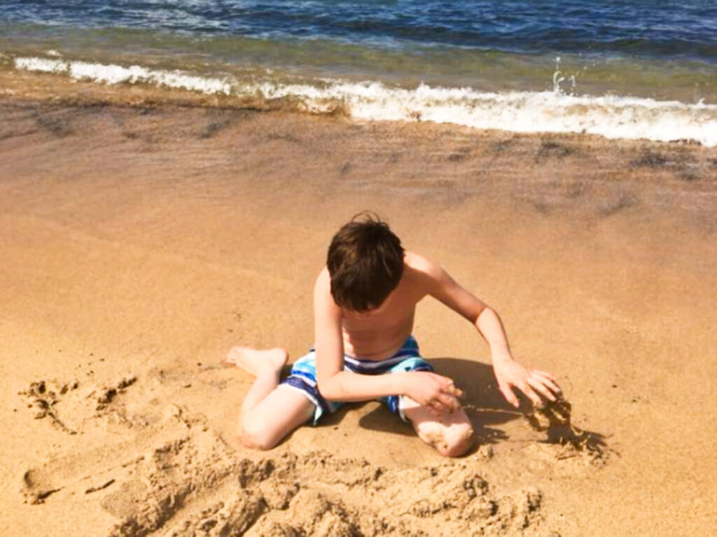 A boy playing the sand at the beach on a sunny day