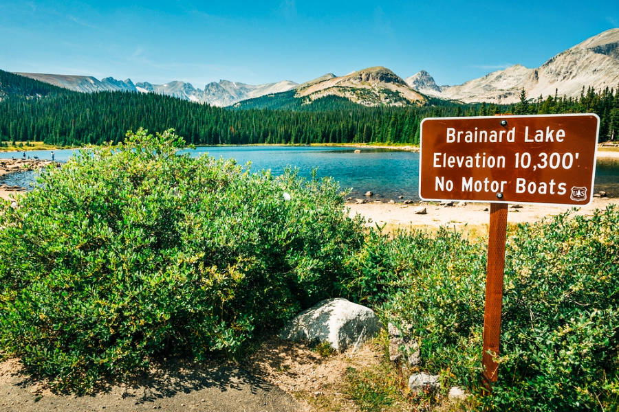 View of the Brainard Lake sign with the scenic views of the Rocky Mountains and lake in the background