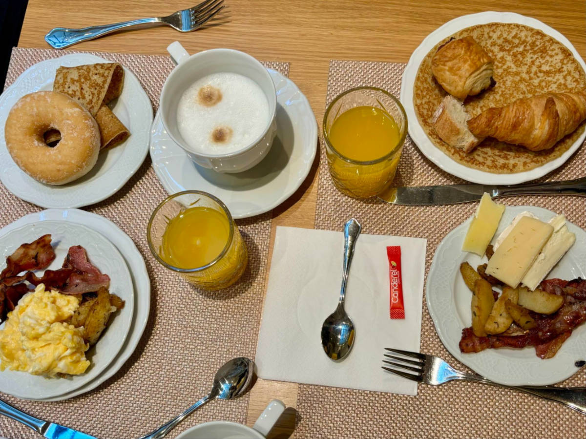 A delicious breakfast of pastries, eggs, cheese, bacon, coffee, and fresh orange juice.