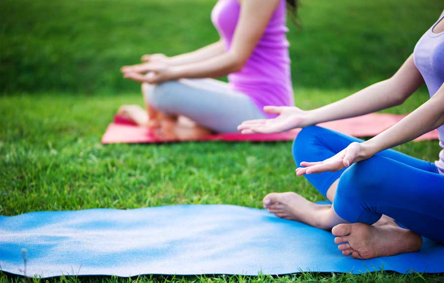 View of two woman having their yoga session on a grass field