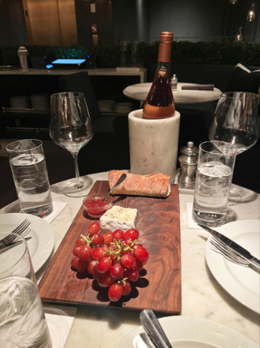 A wooden board with grapes, brie cheese with jam, and a bottle of rosé on the table at RH Rooftop