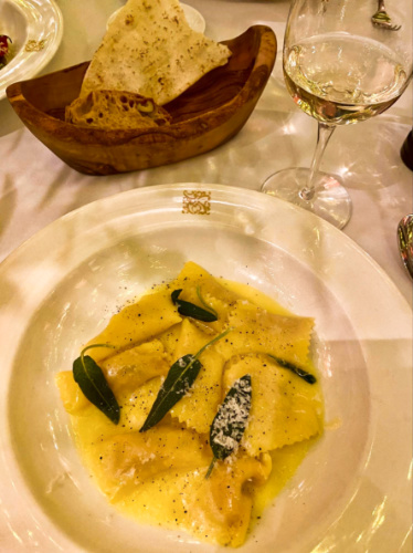 A plate of butternut squash ravioli with a glass of wine and sliced breads on the side from Daphne’s