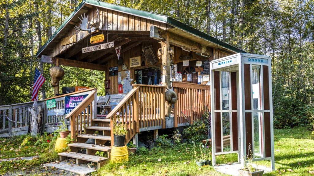 View of the rustic Sourdough Dru's cabin with a telephone booth outside