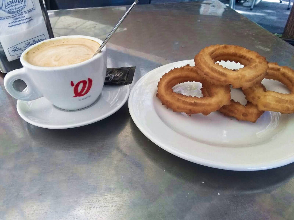 A plate of churros with a cup of cafe con leche