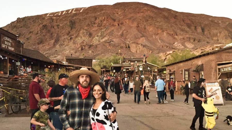 The author McKenna Mobley and a man posing at the Calico Ghost Town with people wandering around in the background