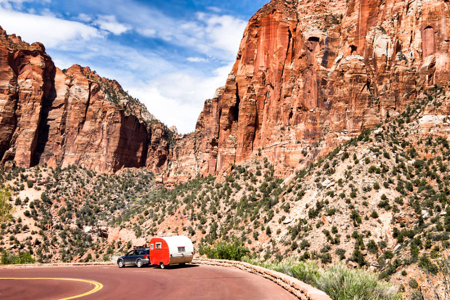 A small red vintage trailer going down the road in Zion National Park