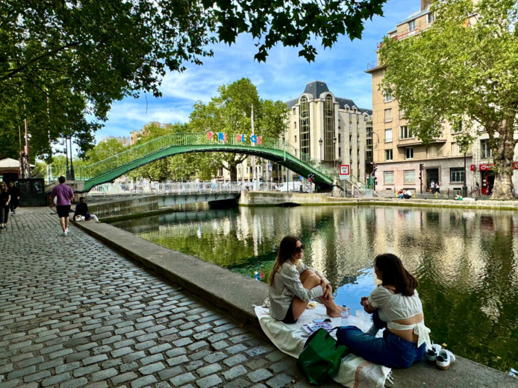 Two young women sitting and talking by the Canal Saint-Martin in the 10th arrondissement on a sunny summer day