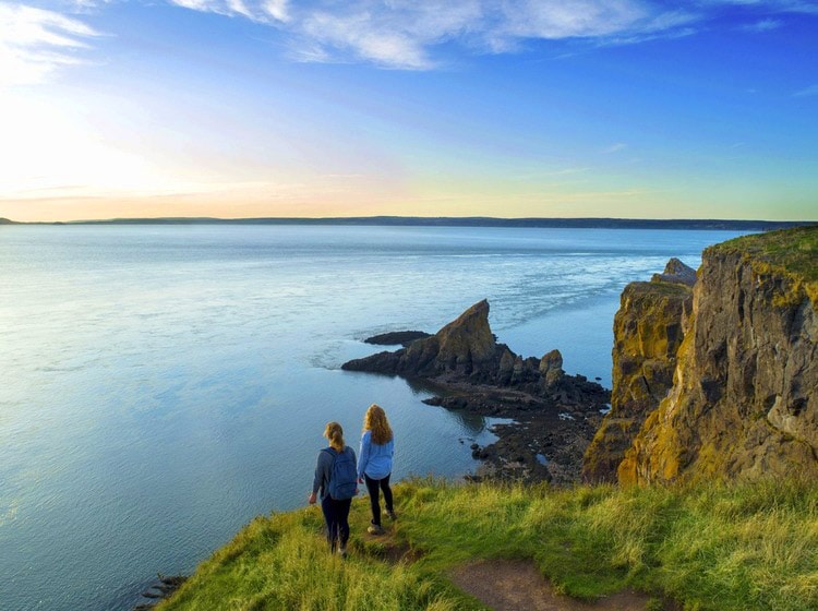 Two girls looking at the wide ocean on a cliff