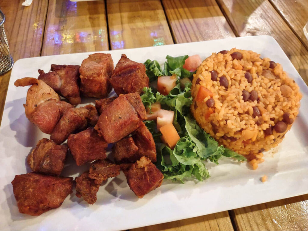 A plate of fried pork with arroz mamposteao and vegetables