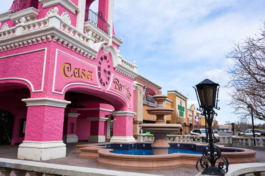 View of the vibrant pink exterior of Casa Bonita in front of the huge fountain and the shops nearby