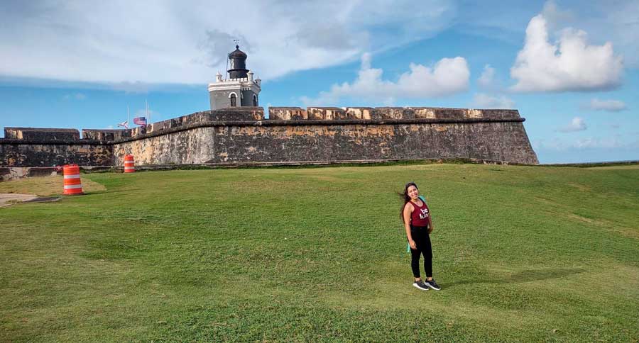 The author smiling for a photo with the Castillo San Felipe del Morro on her background