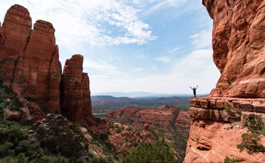 View from a distance of a man posing near the cliff next to Cathedral Rock in Sedona