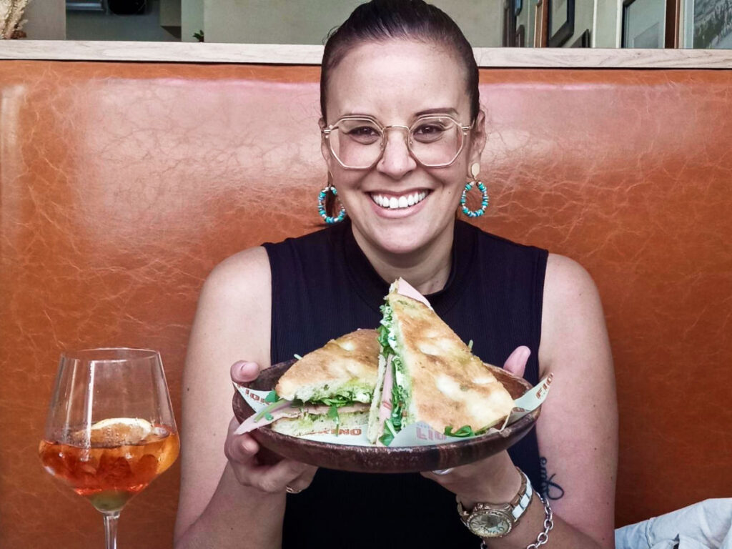 The author Catherine Driver, posing with a plate of sandwiches and a glass of drink from Fiorino