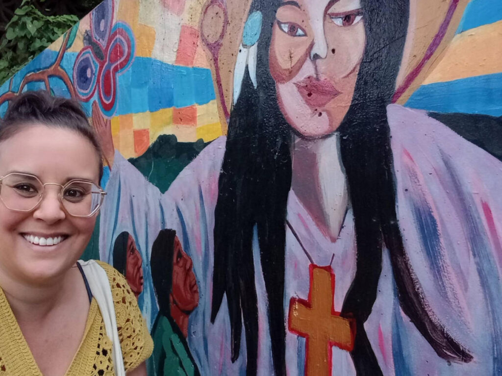 The author Catherine Driver smiling for a selfie with a colorful mural