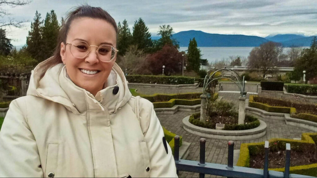 The author Catherine smiling for a photo with an overlooking view of the UBC Rose Garden