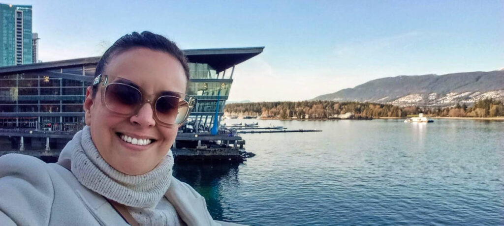 The author Catherine taking a photo with the Stanley Park and the Convention Centre at the waterfront