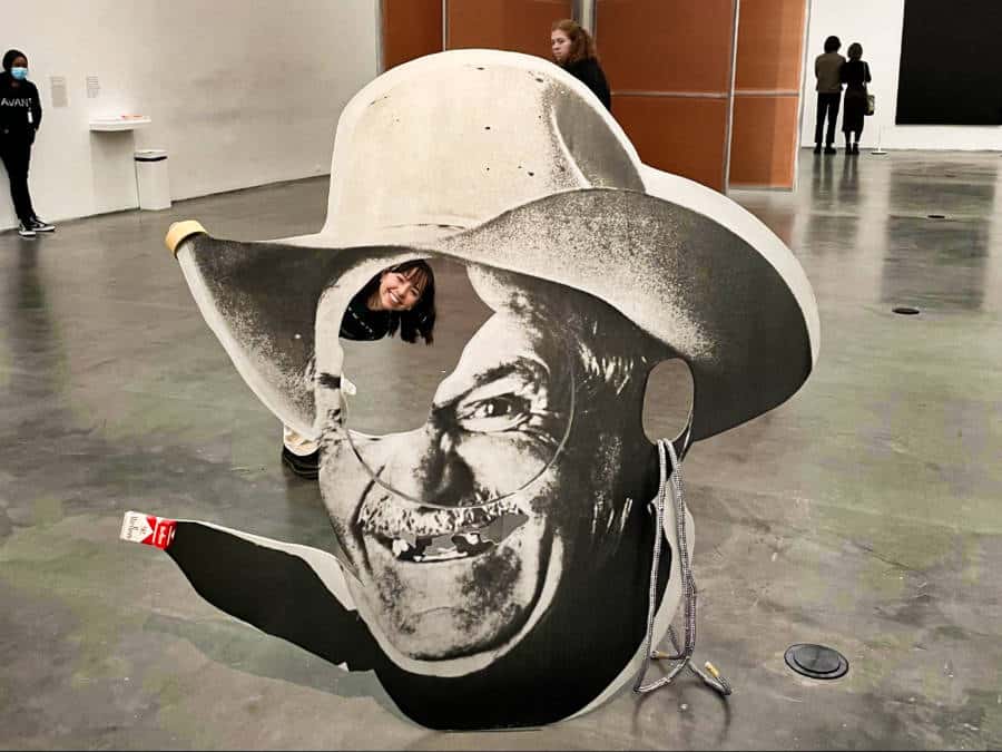 The author Lea Rose Allbaugh peeking at the hole of Chainsaw Cut Cowboy Head by Cady Nolan