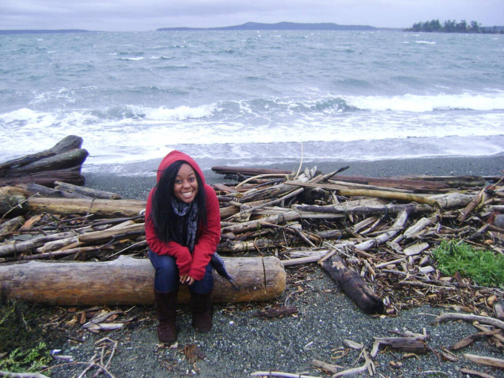 The author, Chelsea Booker sitting on a tree trunk near a beach in San Juan Islands