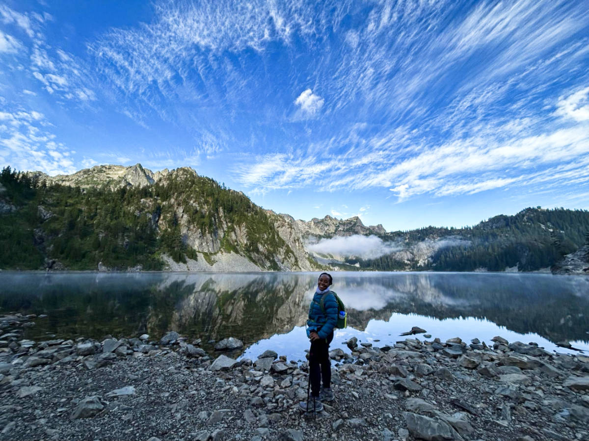 The author Chelsea Booker, posing for a photo with majestic views of the mountain ranges reflecting on the lake in the background