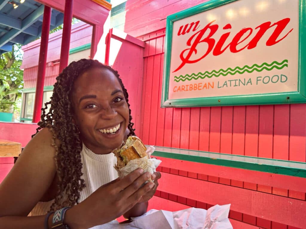 The author Chelsea Booker, posing for a photo while holding a Caribbean roast sandwich at Un Bien
