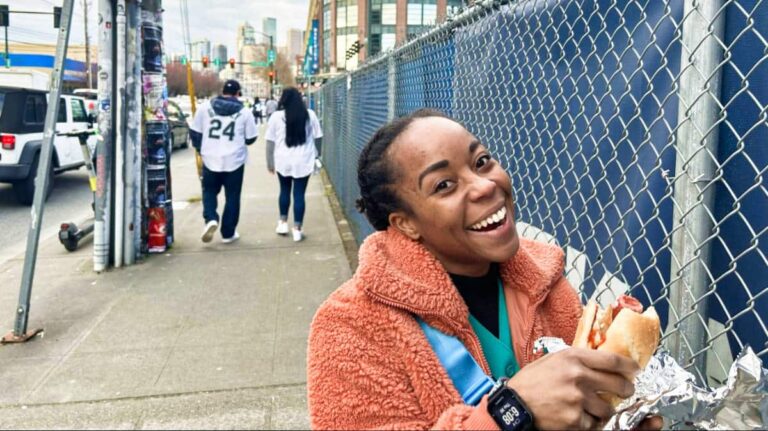 The author Chelsea Booker posing with a hotdog in a bun on the side of the street