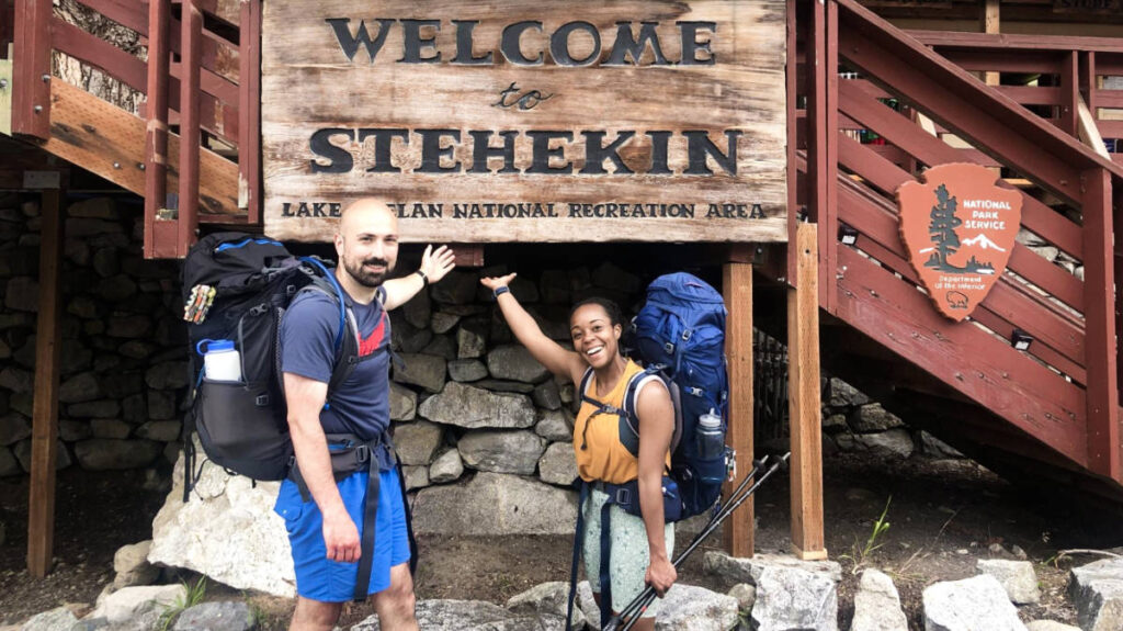 The author Chelsea Booker and her husband pointing the signage of Welcome to Stehekin