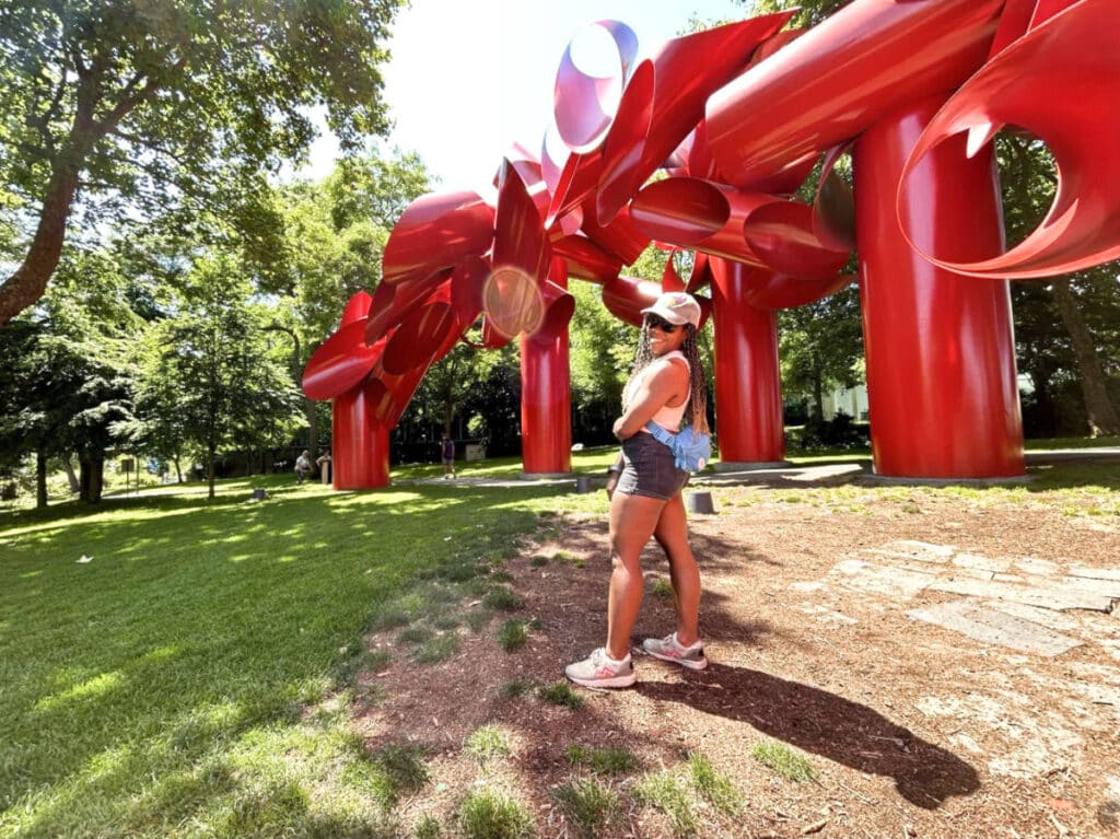 The author Chelsea Booker, posing in front of the unique and bright red sculpture