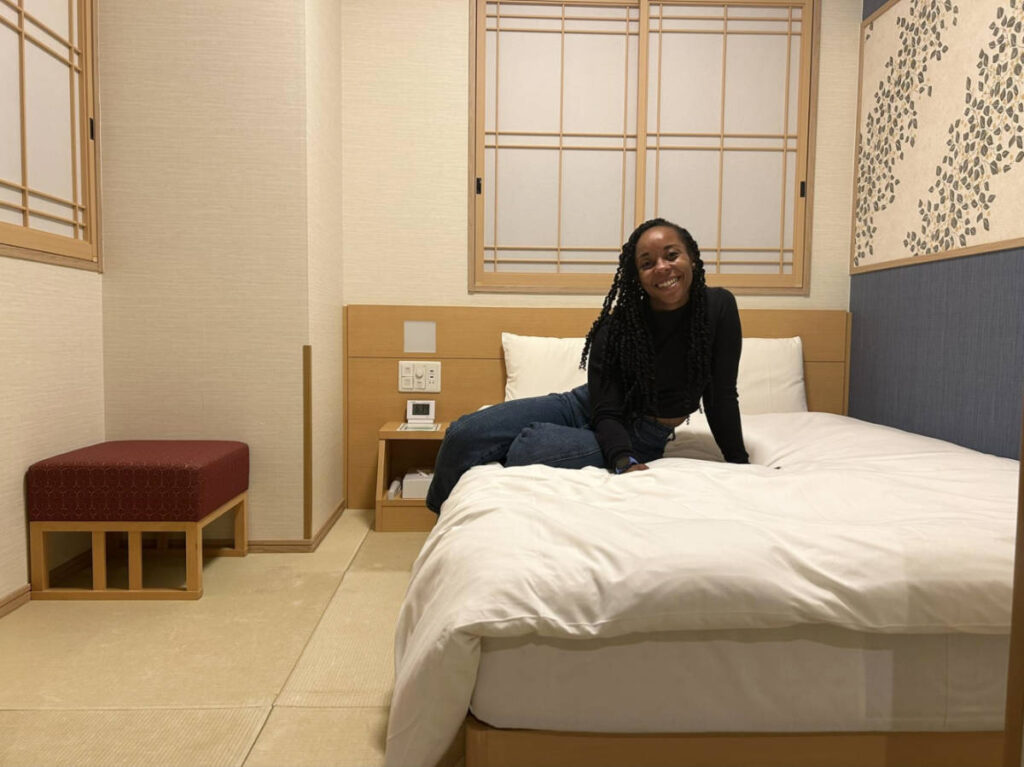 The author Chelsea Booker posing for a photo on the bed of a compact room