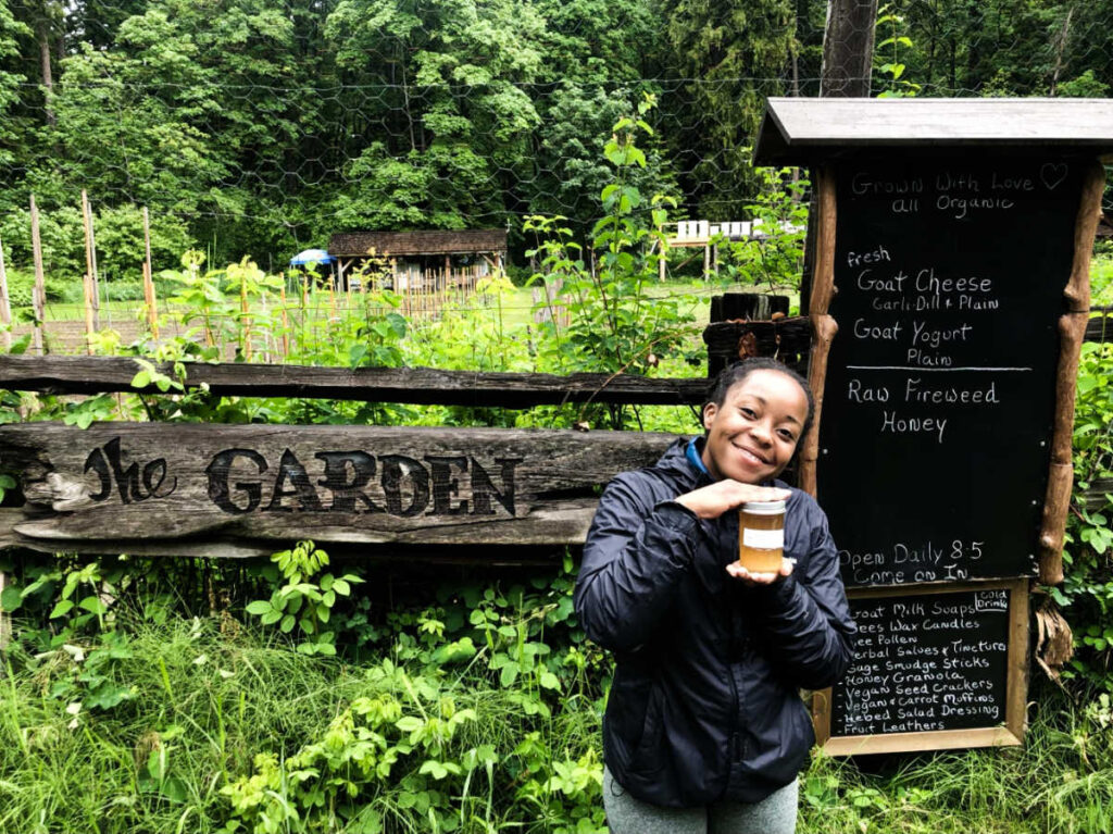 The author Chelsea Booker smiling for a photo while holding a jar of honey at The Garden