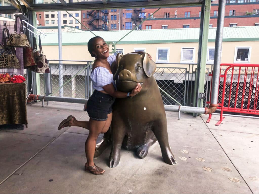 The author Chelsea Booker posing with the bronze market pig statue