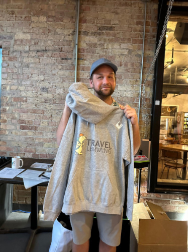 A man smiling for a photo while holding the Travel Lemming hoodie during the Travel Lemming's Chicago Community Meetups