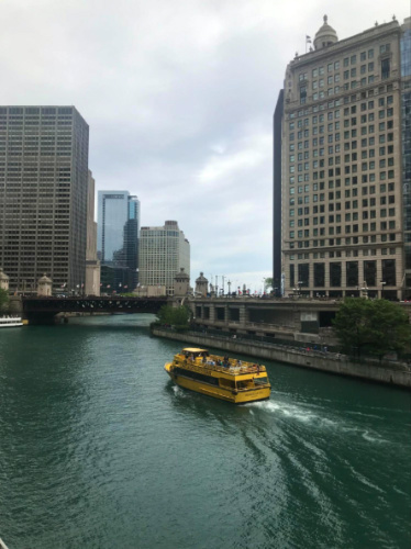 A yellow boat glides along the Chicago River surrounded by urban scenery
