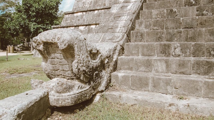 A stone snake head juts out of a pyramid at the site of Chichen Itza